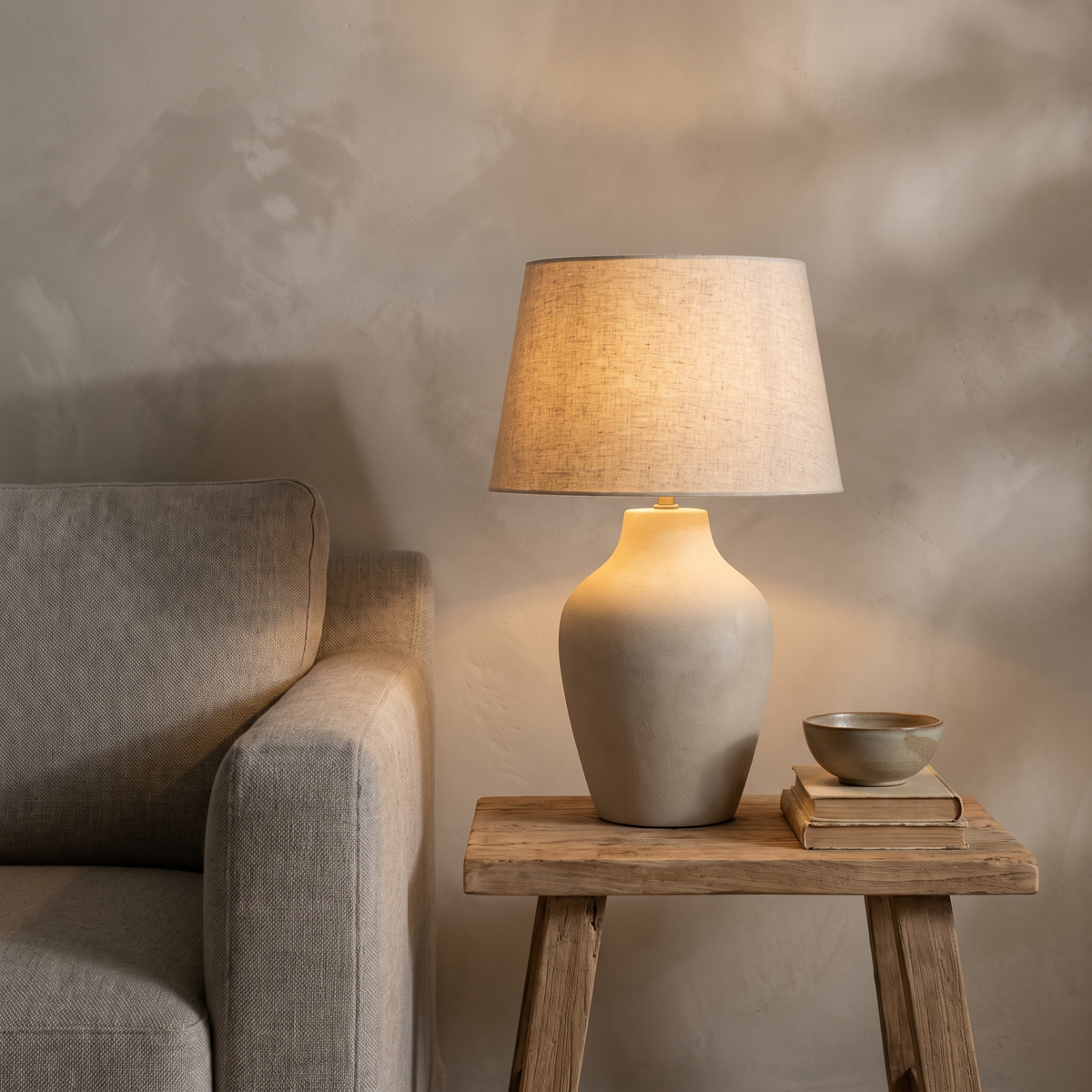 Tänd bordslampa på ett sidobord i ek bredvid en linnesoffa