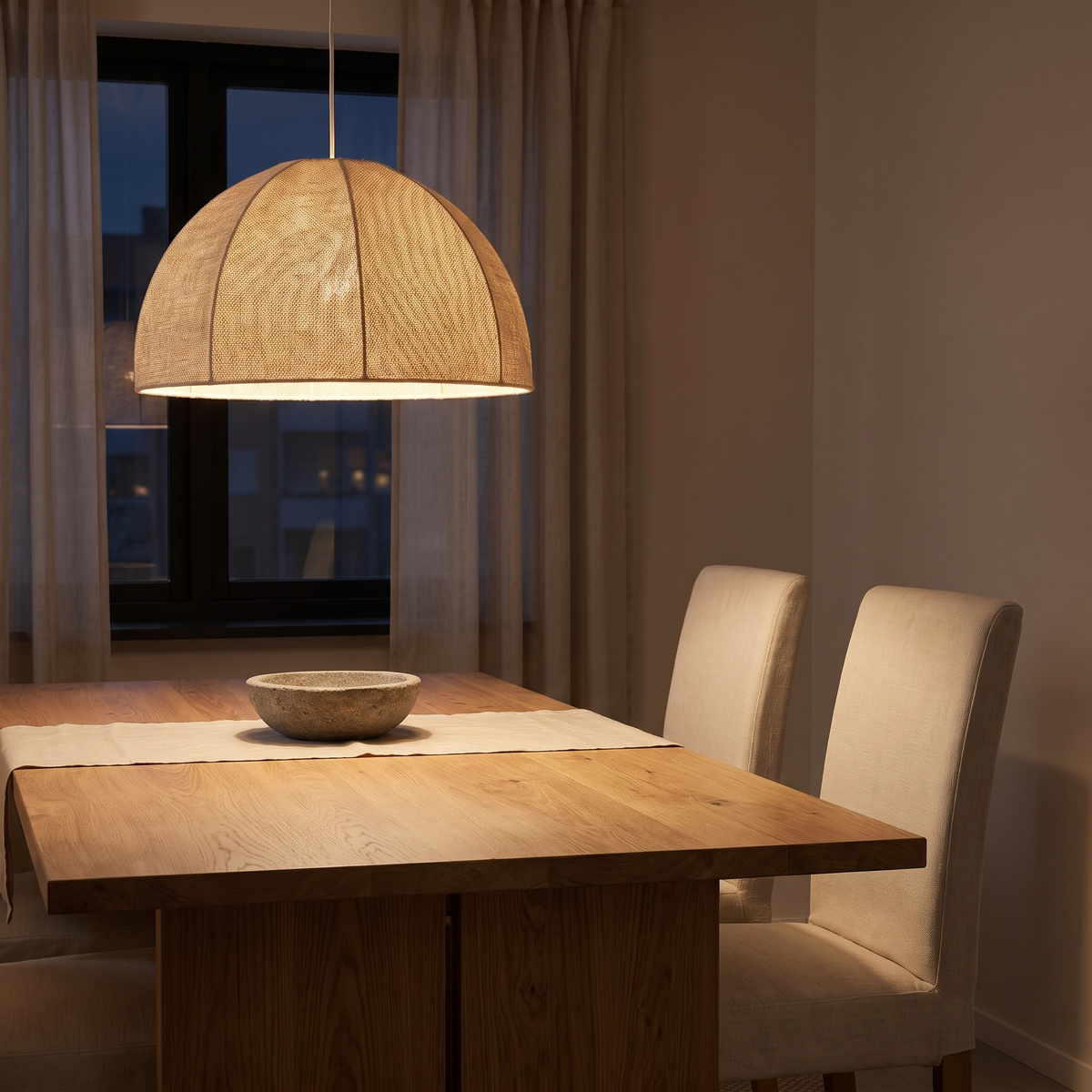 Pendellampa i textil som hänger lågt över ett matbord i ek på kvällen